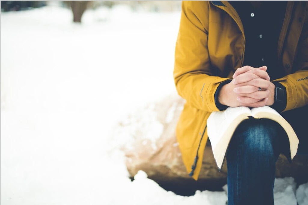 closeup shot person sitting rock with bible knee praying